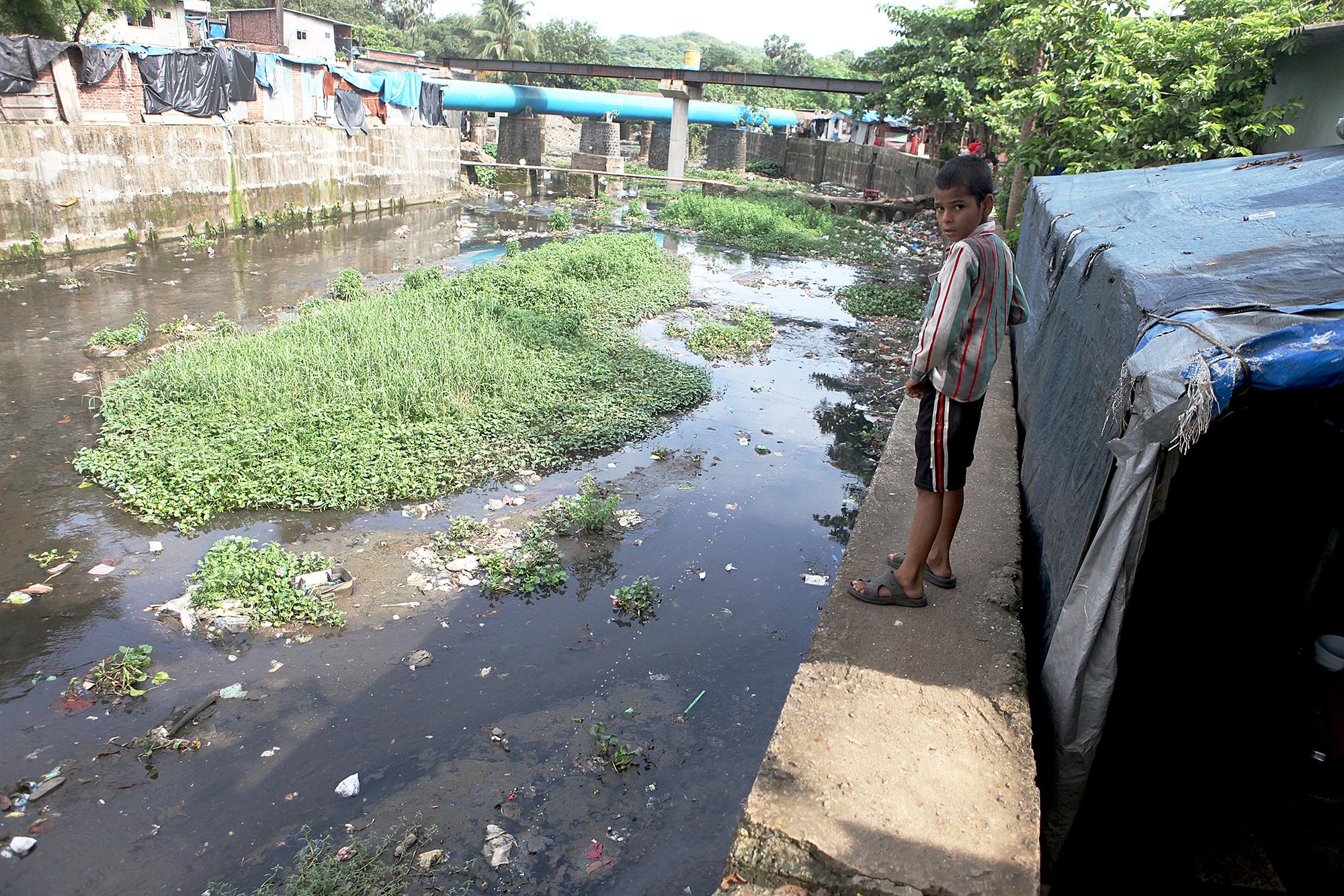 A young boy urinates in the Mithi river while walking back home in Bhim Nagar