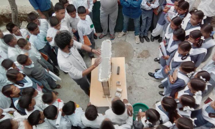 Children gather around Ashvath Singh as he demonstrates hydrogeology.